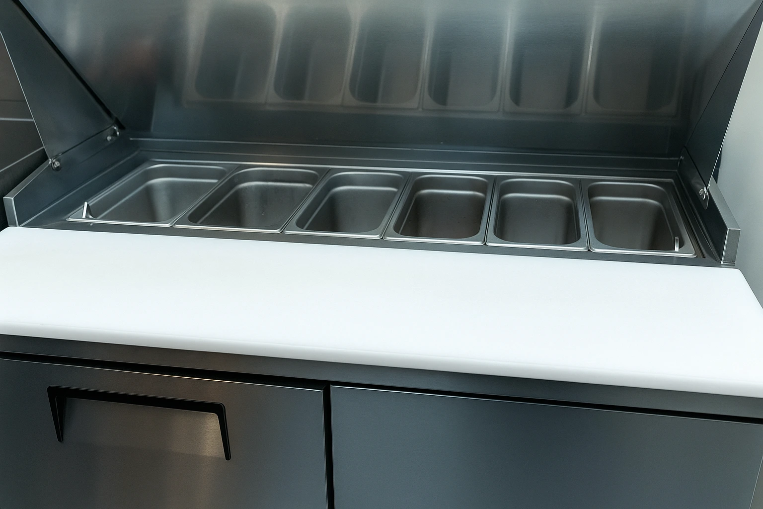 Close-up view of a commercial sandwich prep table with open ingredient bins and stainless steel workspace, photographed in a professional kitchen setting.
